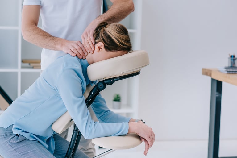 Male therapist performing chair massage for businesswoman in office setting