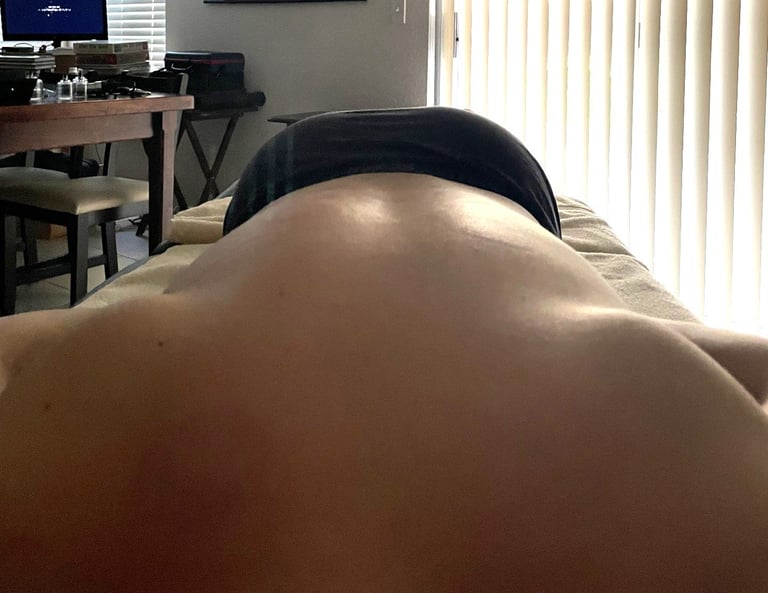 Person bent forward indoors showing back and shoulders, wearing dark underwear, with office setting visible in background
